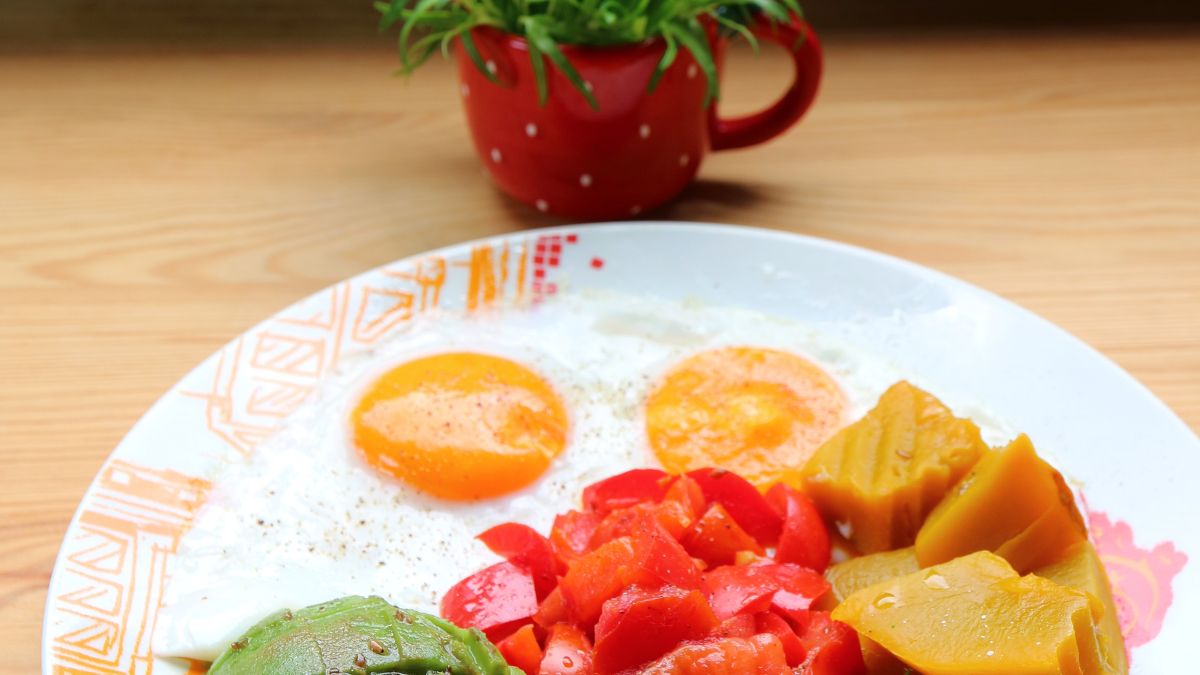 Piatto colorato con uova, pomodori, avocado e verdure cotte.