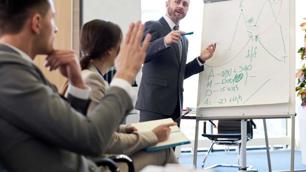 Un formatore spiega concetti su una lavagna a un gruppo di professionisti.