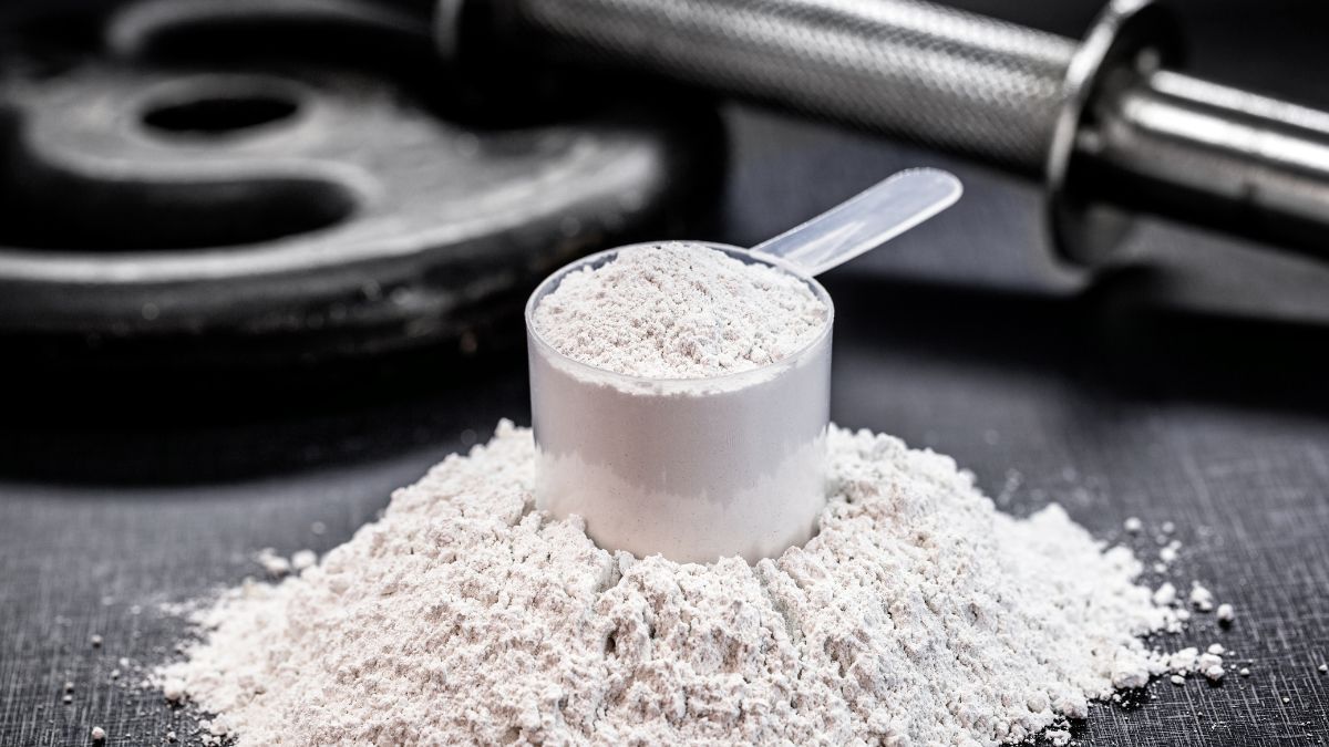 Un misurino di creatina in polvere su un fondo scuro con attrezzi da palestra.