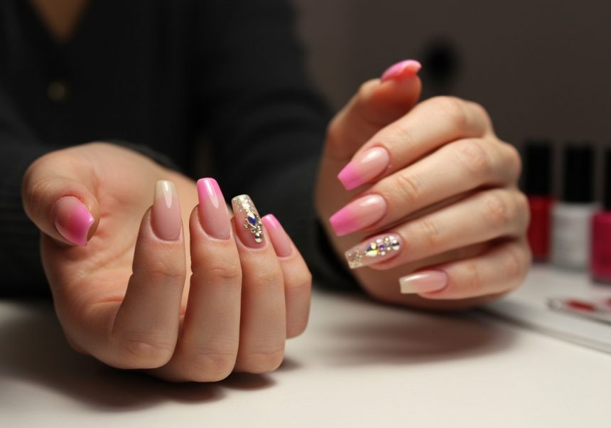Mani con unghie ricostruite in diverse tonalità di rosa e decorazioni.